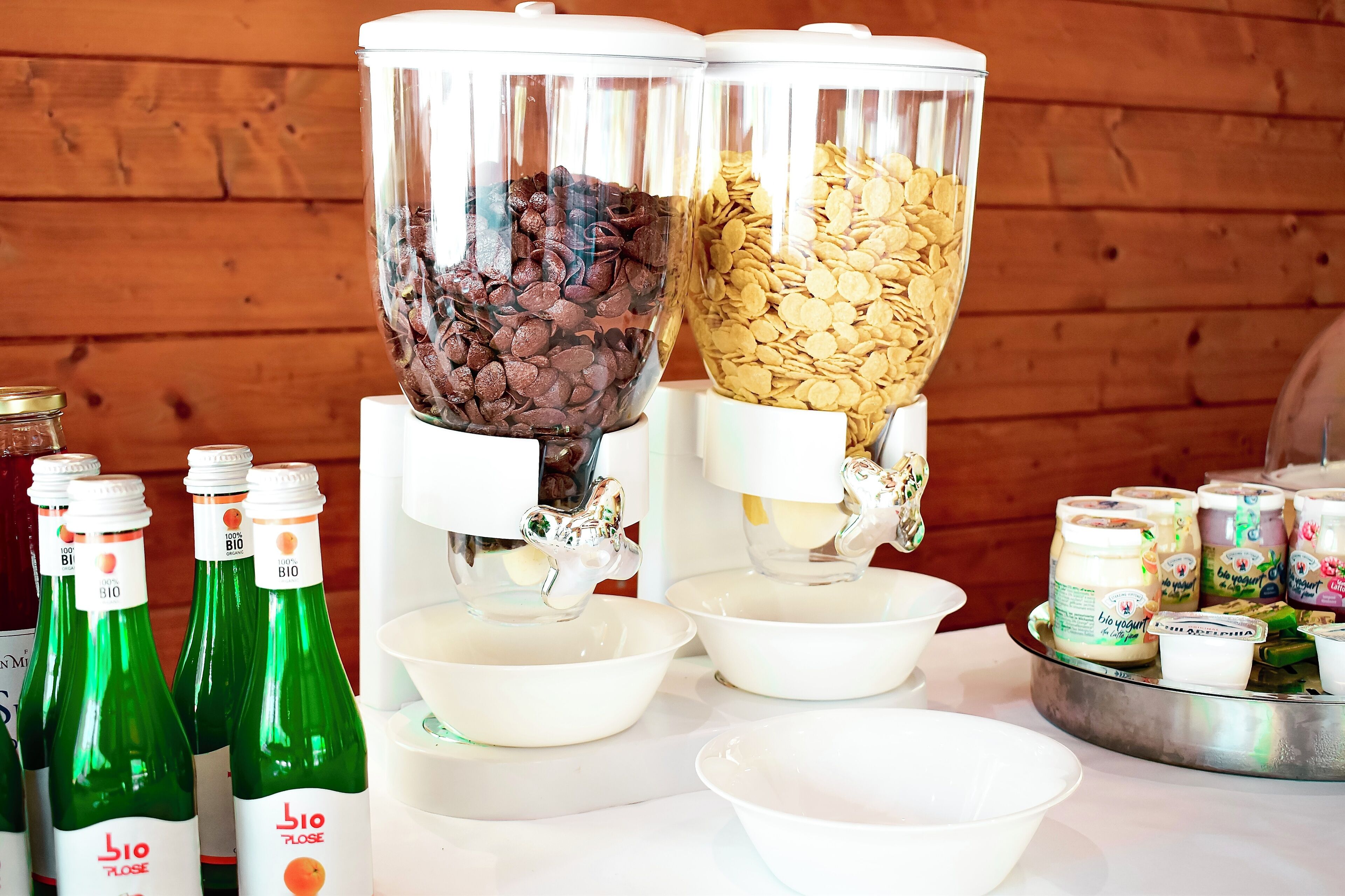 A food dispensing station with two containers, one with chocolate chips and the other with cereal flakes, and several bottles of organic juice.