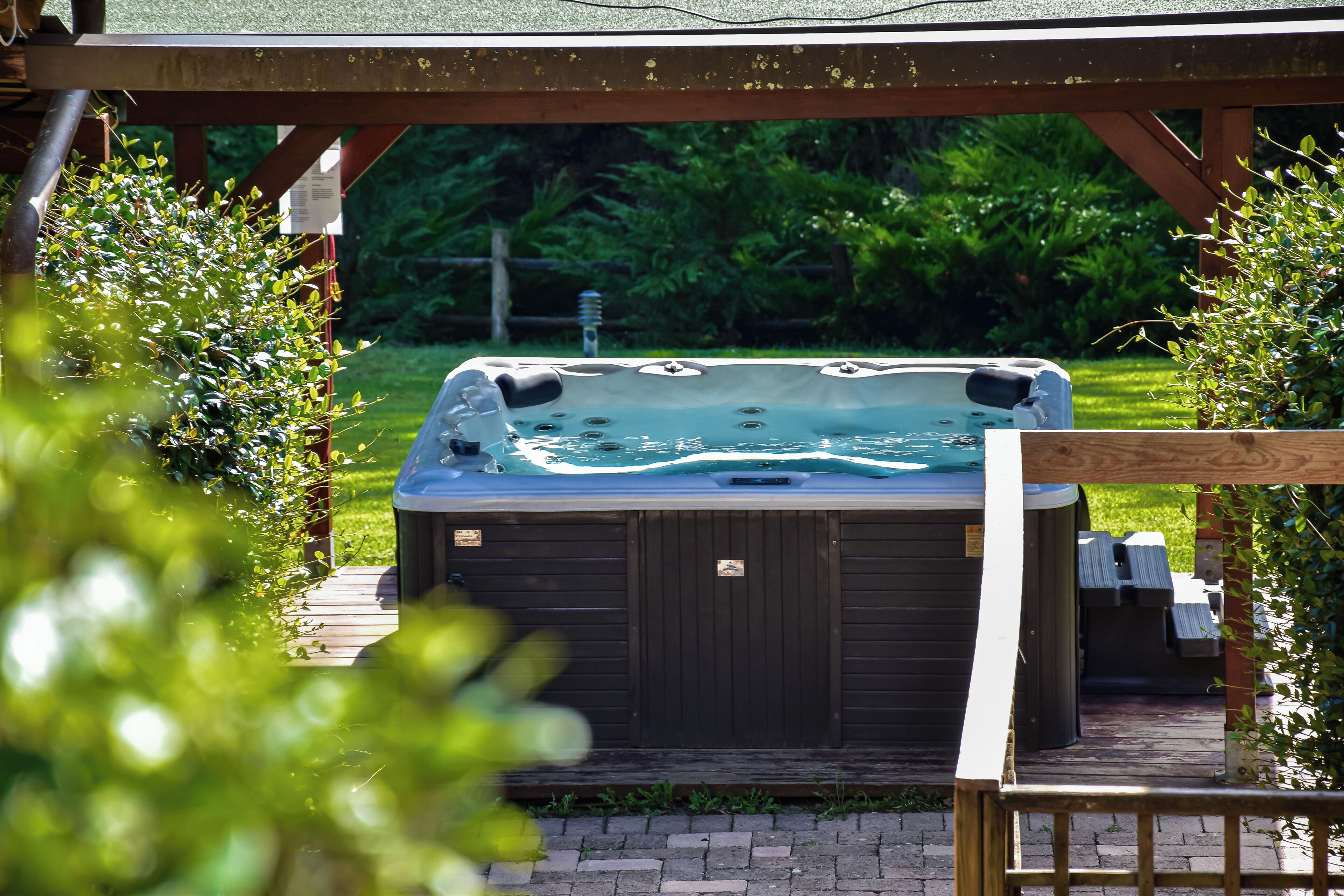 A hot tub under a wooden pergola with a grassy yard in the background.