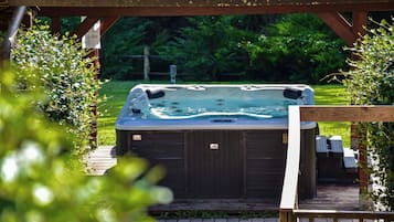 A hot tub under a wooden pergola with a grassy yard in the background.