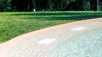 A clear pool with a curved edge, surrounded by a well-maintained grassy area and dense foliage in the background.