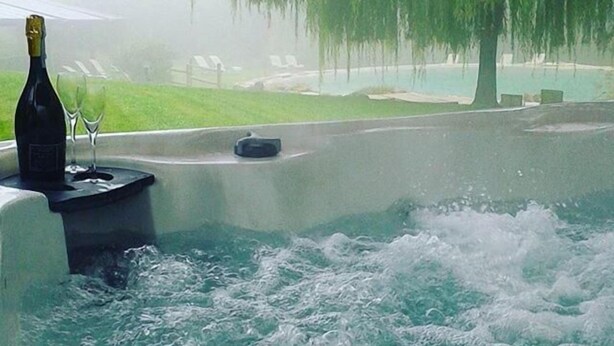 A hot tub with a bottle and glasses, surrounded by a misty outdoor area with trees and a pool. - Lebbiano Residence Bio Resort  (Scandicci)