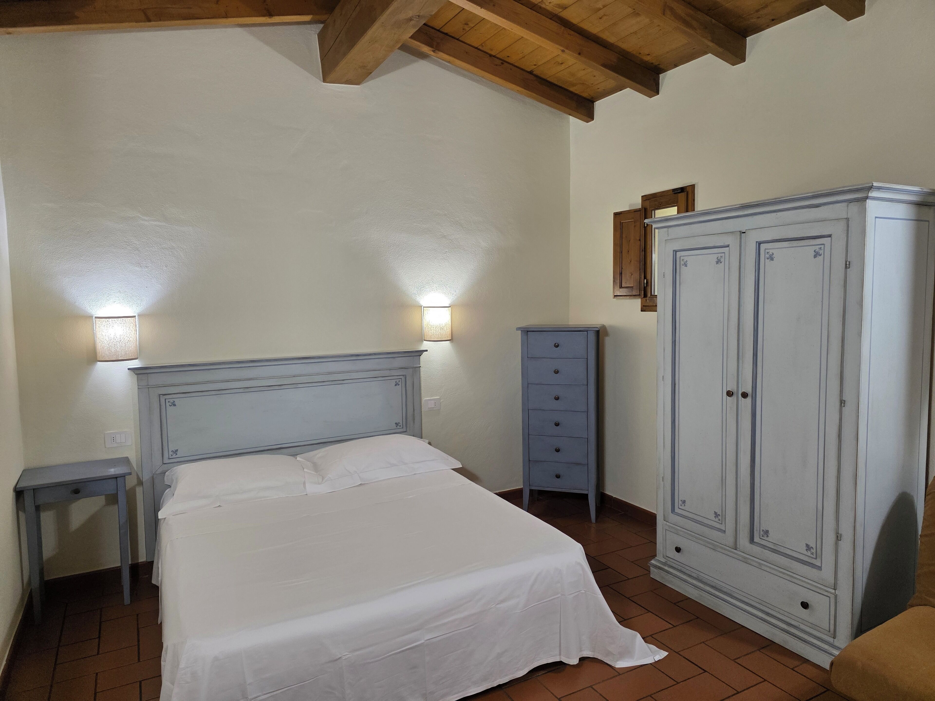 Une chambre à coucher comprenant un lit, une armoire, une table de chevet et deux lampes fixées au mur.