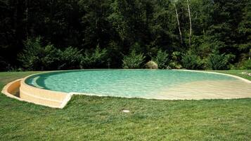 Una piscina circular con un borde de césped y un bosque de fondo.