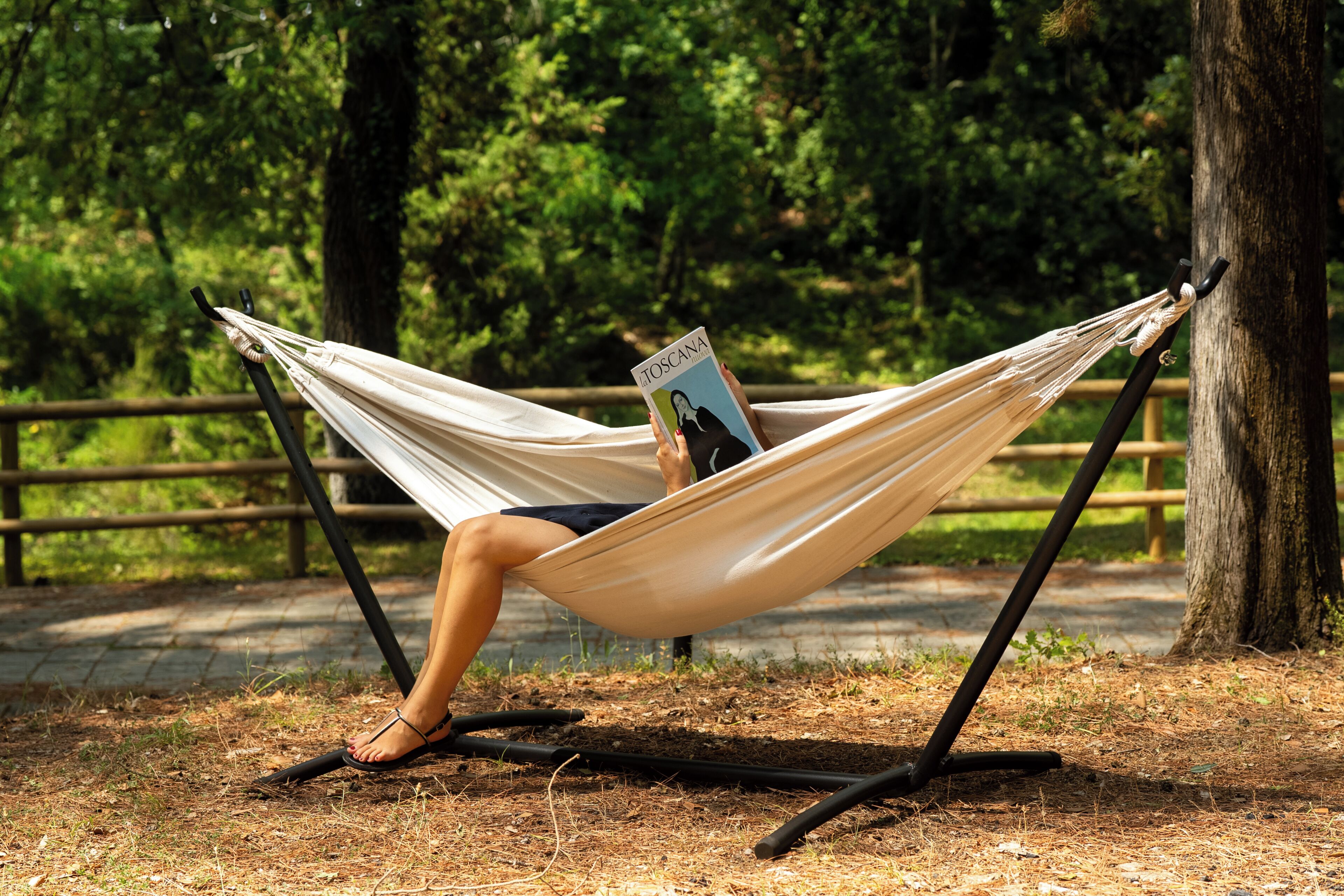 Un hamac est installé sur un support en bois dans un parc, avec des arbres en arrière-plan.