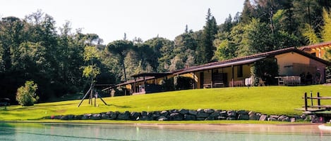 A pool with a stone border, a grassy area, and a building with a sloped roof.