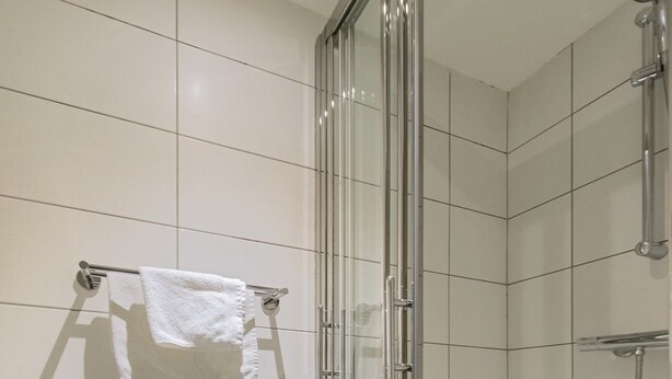 A modern bathroom with white tiled walls, a glass shower enclosure, and a towel rack with a white towel. - B&B De Hofnar Maastricht (Maastricht)
