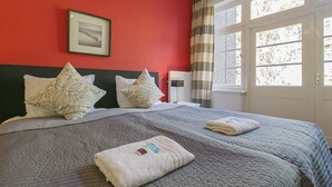 Habitación de hotel con una pared roja, un cuadro enmarcado, una cama con colcha gris y una ventana con cortinas.