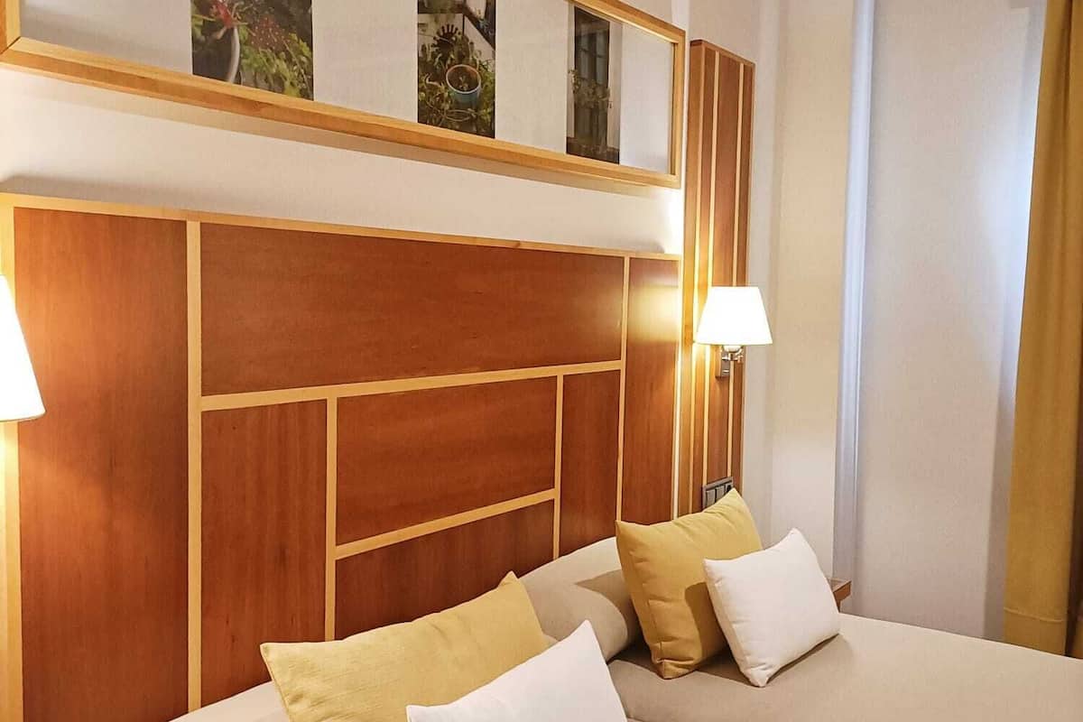 A hotel room with a large bed, wooden headboard, and a view of a garden through a window.