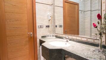 A bathroom with a wooden door, a marble sink, a mirror, and a vase with flowers.