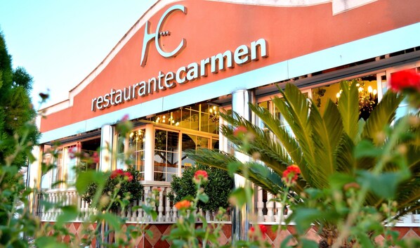 A restaurant named 'restaurantecarmen' with a modern facade, large windows, and a balcony with potted plants. - Hotel Carmen (La Carlota)