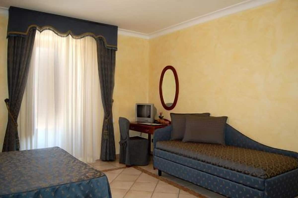 A hotel room with a bed, a sofa, a desk with a computer, and a mirror.