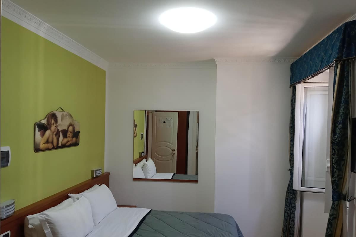A hotel room with a bed, a mirror, a green wall, and a window with curtains.