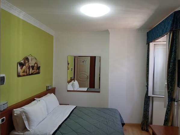 A hotel room with a bed, a mirror, a green wall, and a window with curtains. - GuestLa Casa dell'Arte (Rome)