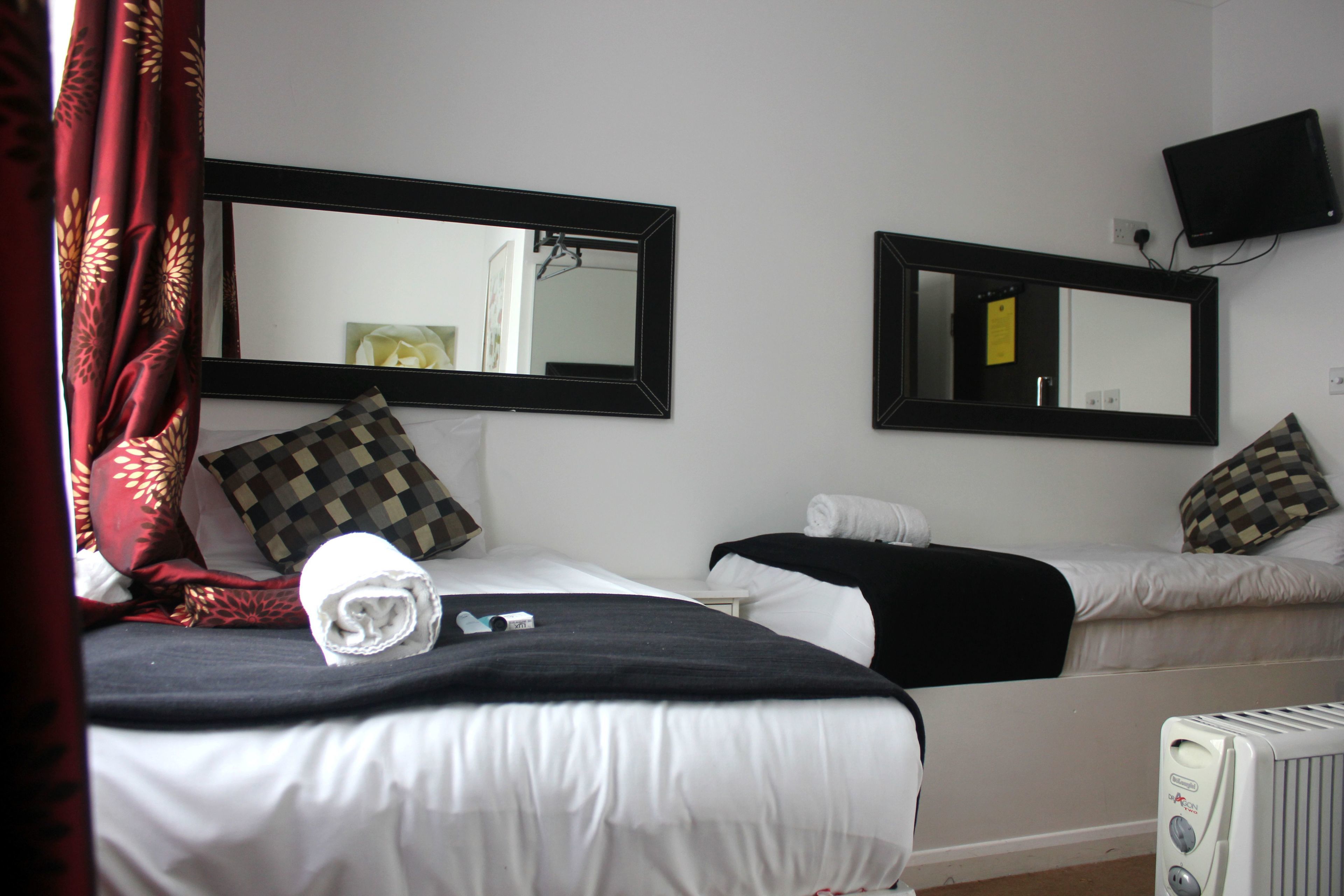Habitación de hotel con dos camas, un televisor montado en la pared y un calefactor en el suelo.