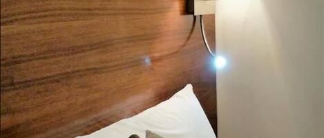 Un lit bien fait, recouvert d’une couverture à carreaux, avec une tête de lit en bois et une lampe de chevet.