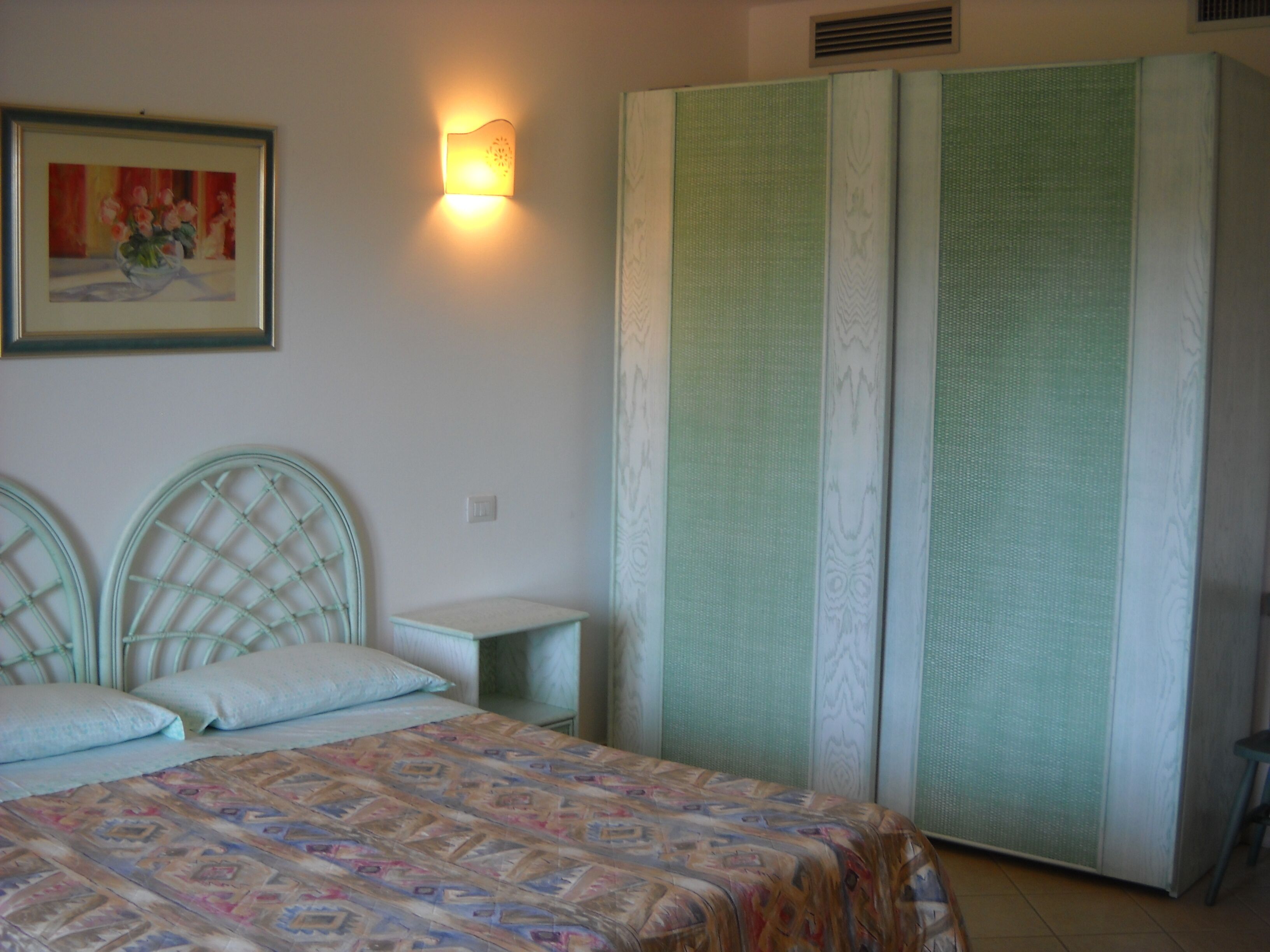 Un dormitori amb un llit, dues taules de nit, un armari i una làmpada penjada a la paret.