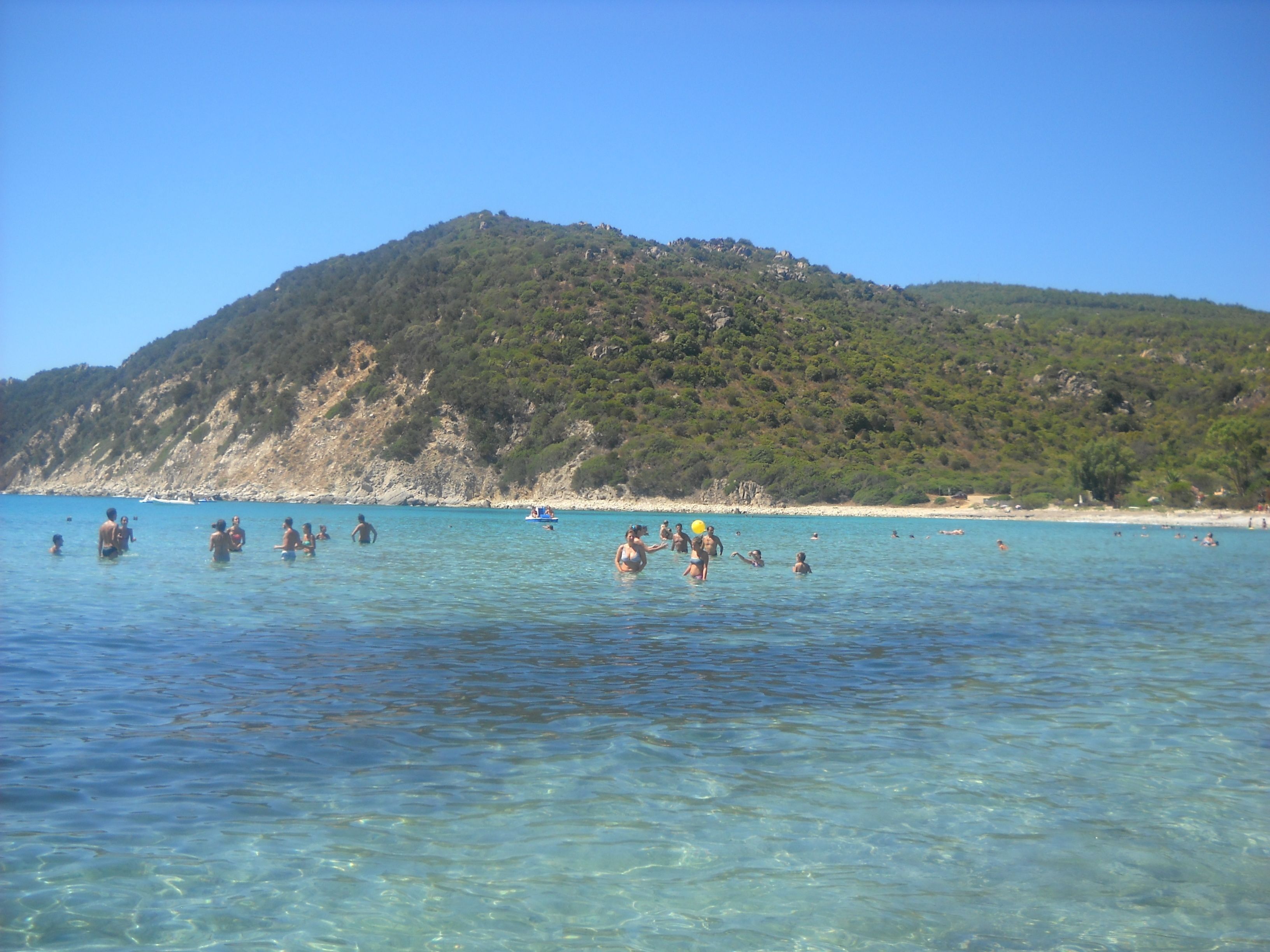 Una playa con agua cristalina y un paisaje montañoso al fondo.