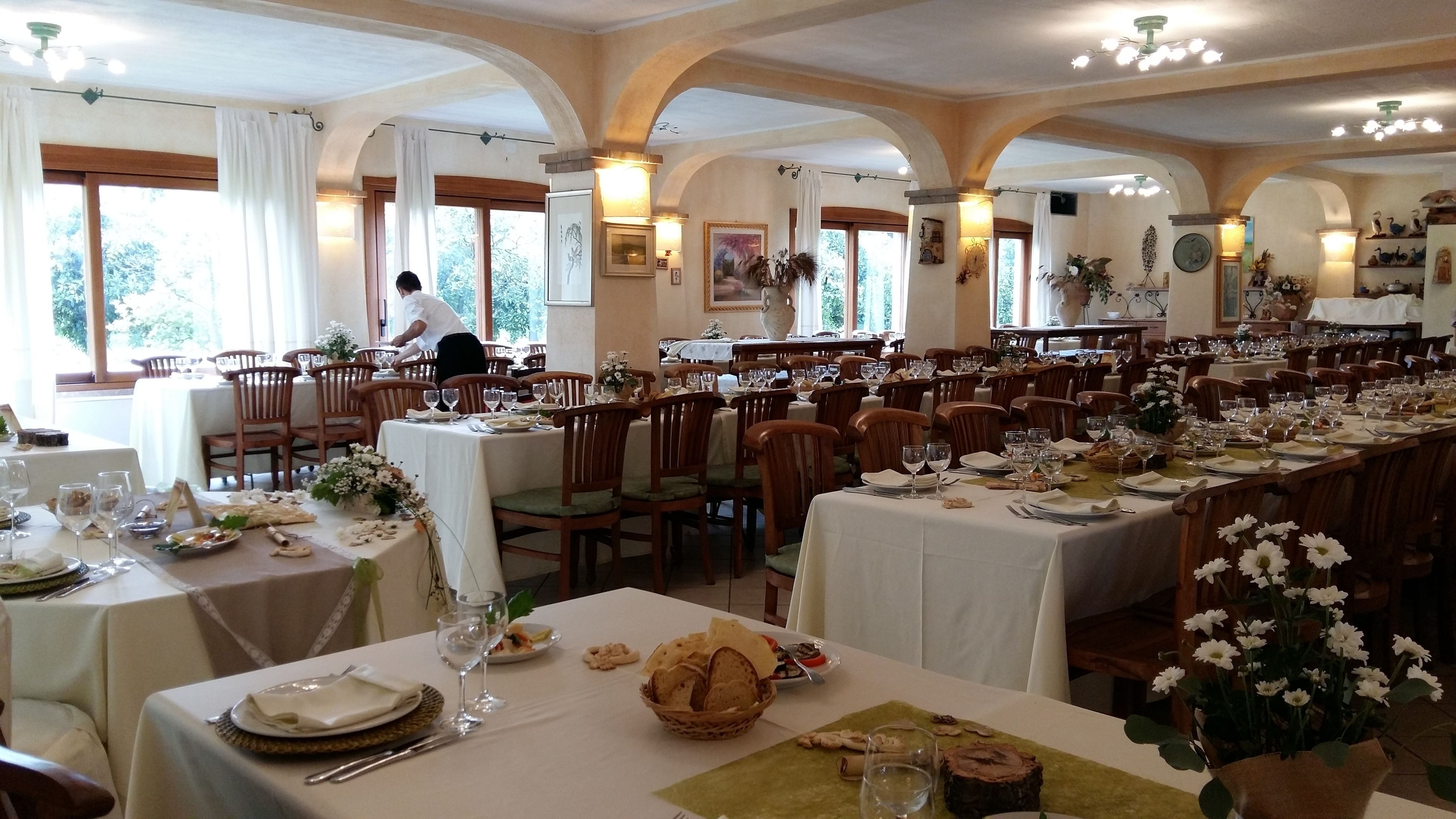A restaurant with multiple tables set for dining, featuring white tablecloths and wooden chairs.