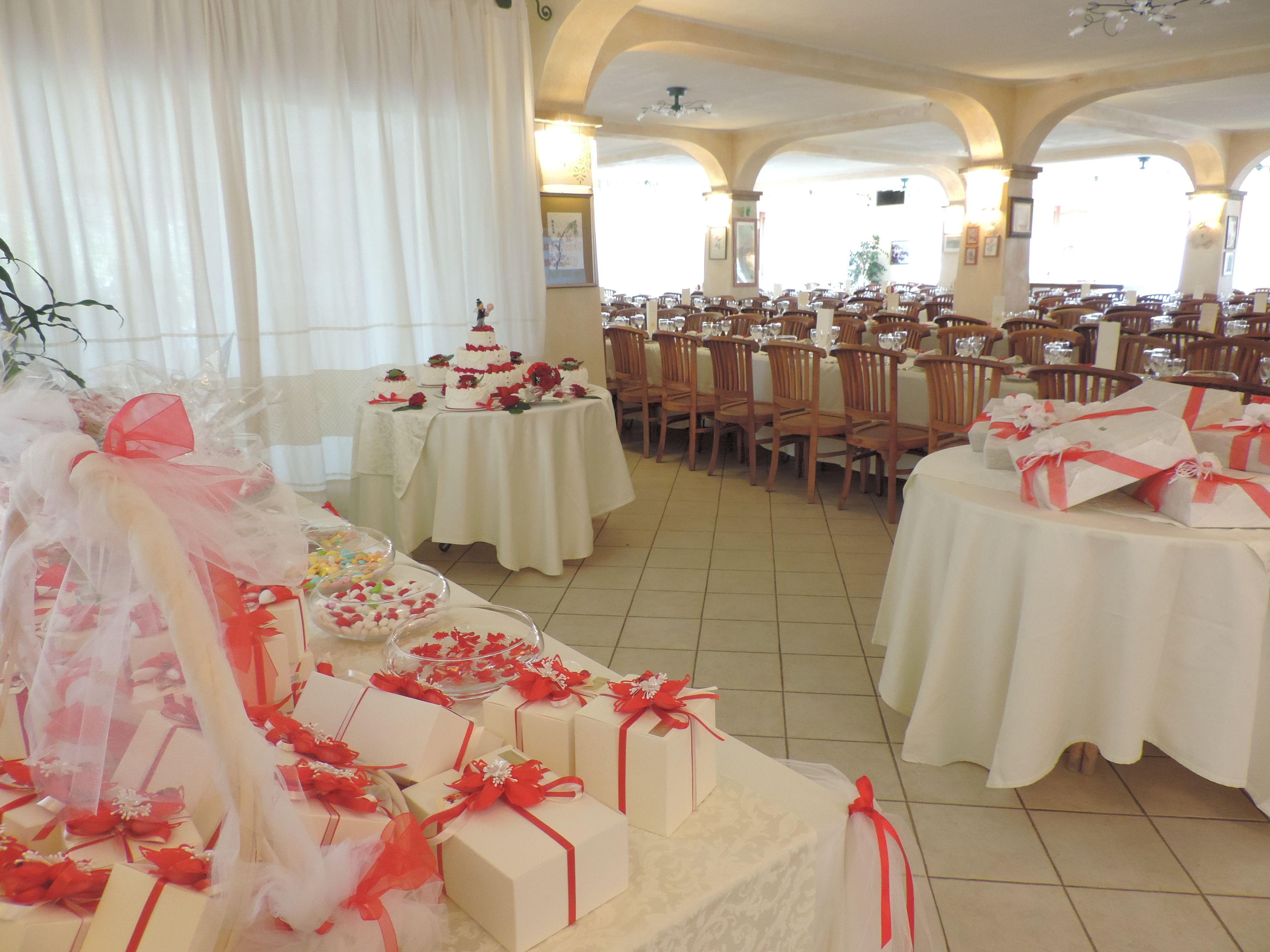 A banquet hall with round tables covered in white tablecloths, chairs arranged around them, and a tiered wedding cake on one table.