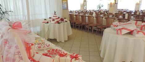 A banquet hall with round tables covered in white tablecloths, chairs arranged around them, and a tiered wedding cake on one table.