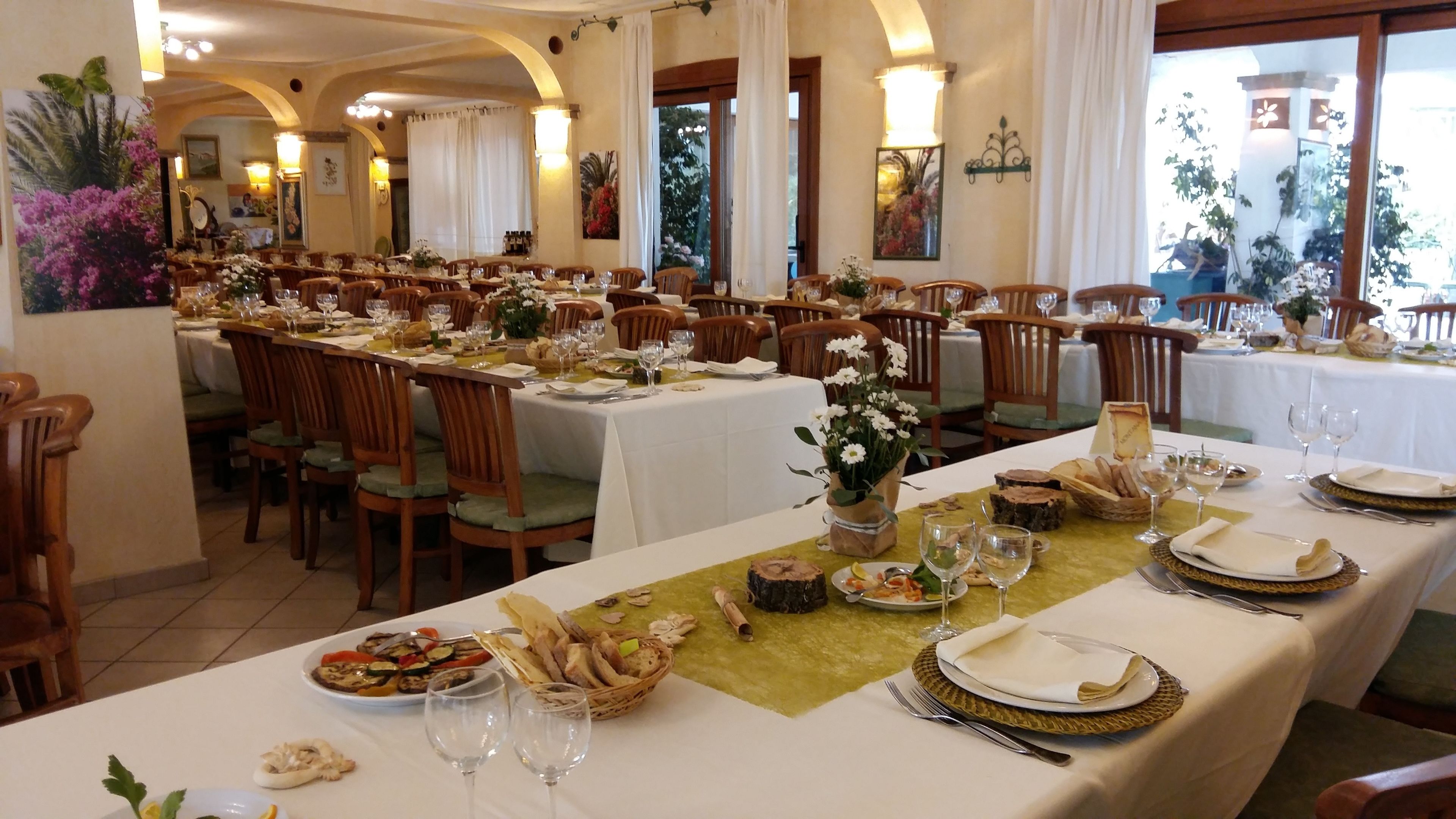 Ein Restaurant mit mehreren gedeckten Tischen, weißen Tischdecken, Holzstühlen sowie verschiedenen Speisen und Getränken.