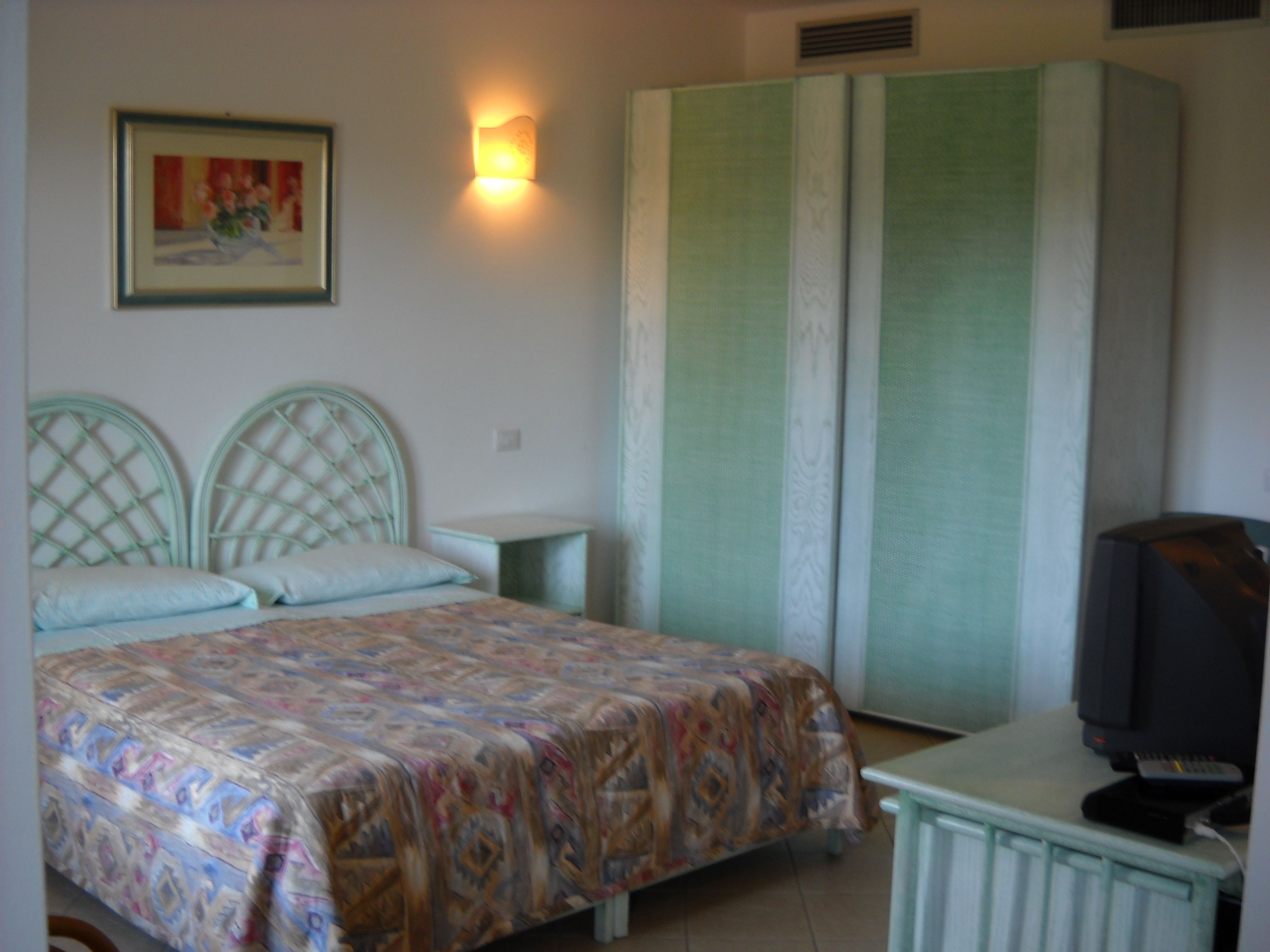 Ein Schlafzimmer mit einem Bett, einem Fernseher, einem Kleiderschrank und einem Bild an der Wand.