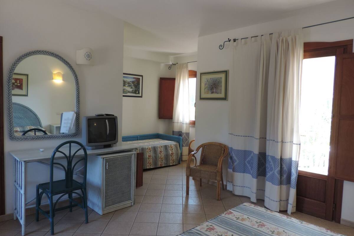 Ein Zimmer mit einem Bett, einem Schreibtisch mit Stuhl, einem Fernseher und einem Fenster mit Vorhängen.