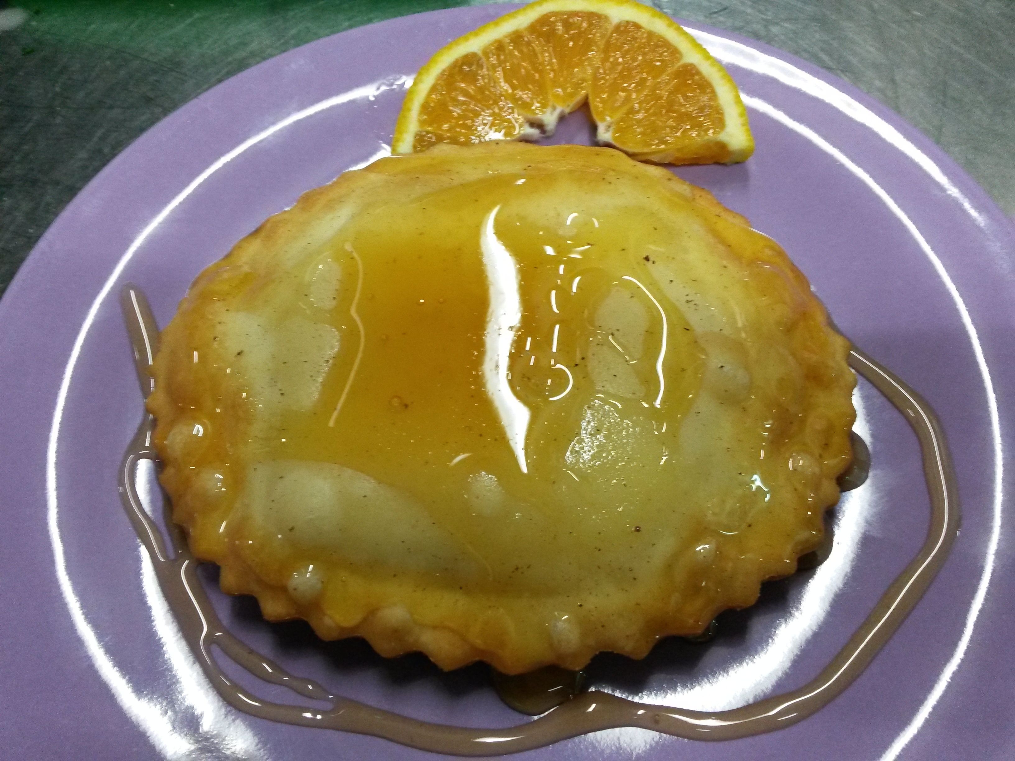 Un postre sobre un plato morado con una rodaja de naranja y almíbar.
