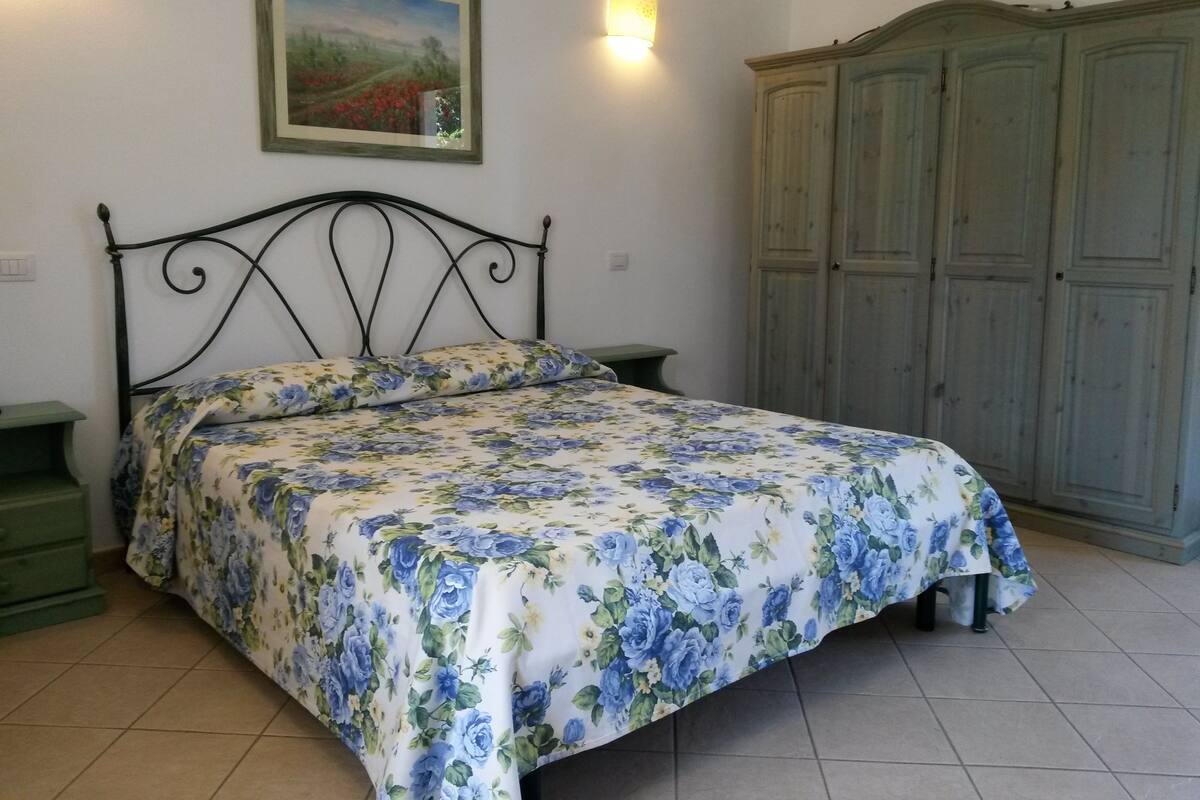 Ein Schlafzimmer mit einem Bett, einem Nachttisch, einer grünen Kommode, einem Kleiderschrank und einer Wandlampe.