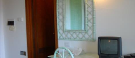 A room with a wooden door, a mirror with a green frame, a television on a cabinet, and a chair.