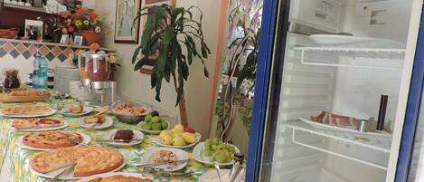 Una mesa de buffet con diversos platos, un refrigerador y una planta decorativa.