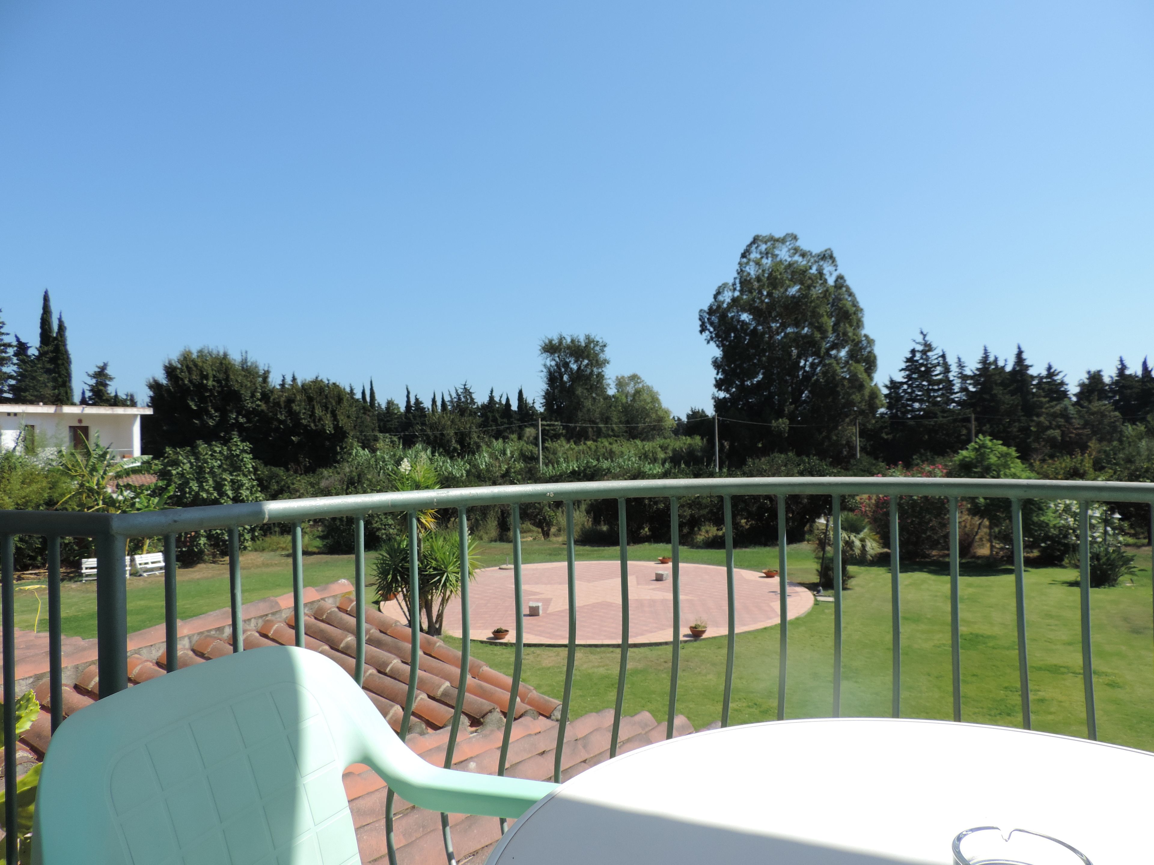 A balcony with a view of a circular patio area, surrounded by greenery and trees.