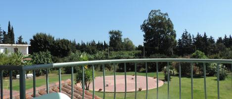 A balcony with a view of a circular patio area, surrounded by greenery and trees.