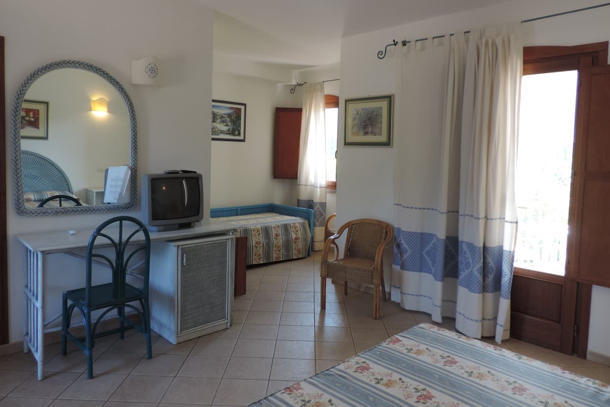 Ein Zimmer mit einem Bett, einem Schreibtisch mit Stuhl, einem Fernseher und einem Fenster mit Vorhängen.