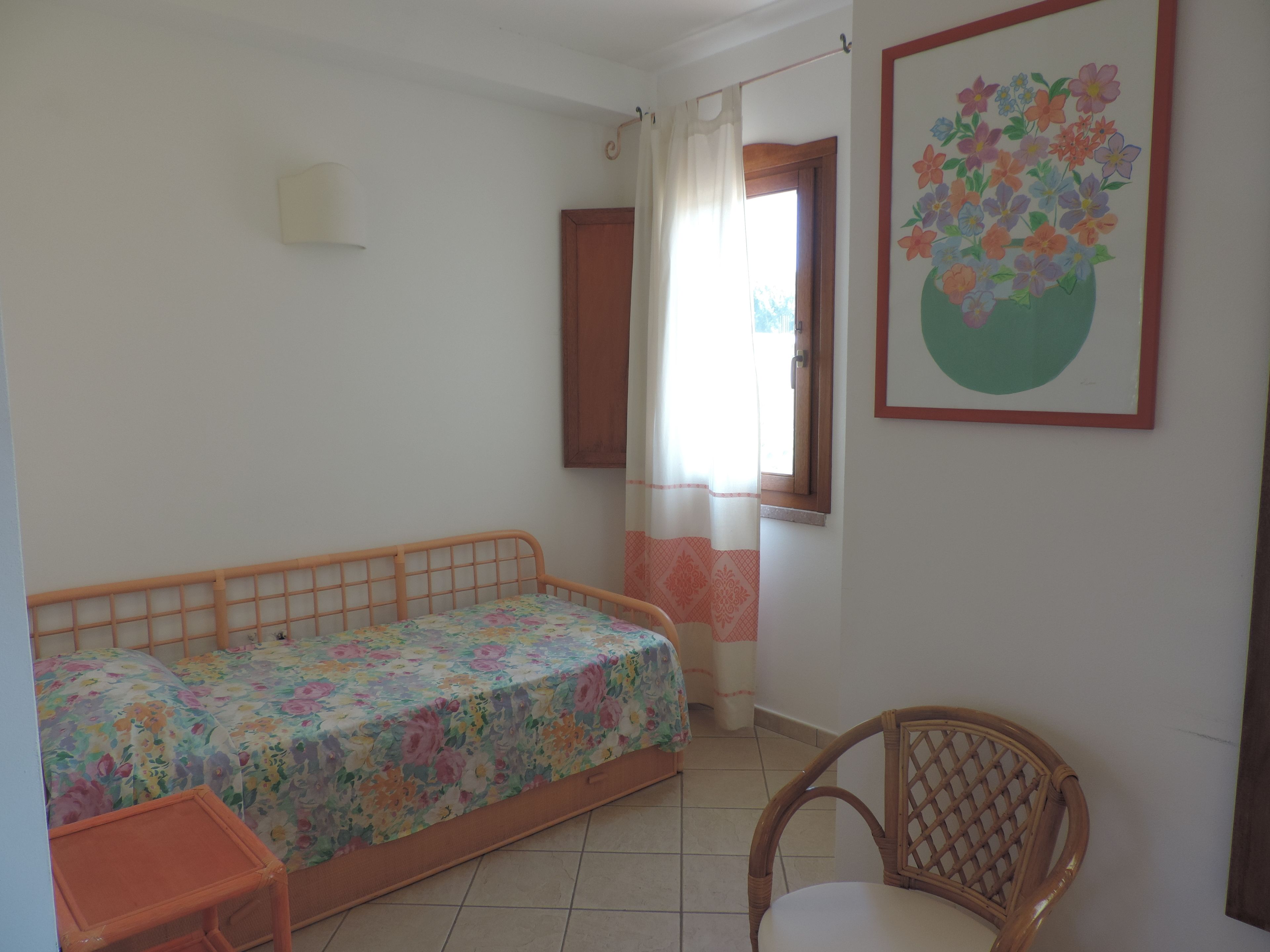 A bedroom with a bed, a chair, a window, and a wall-mounted picture.