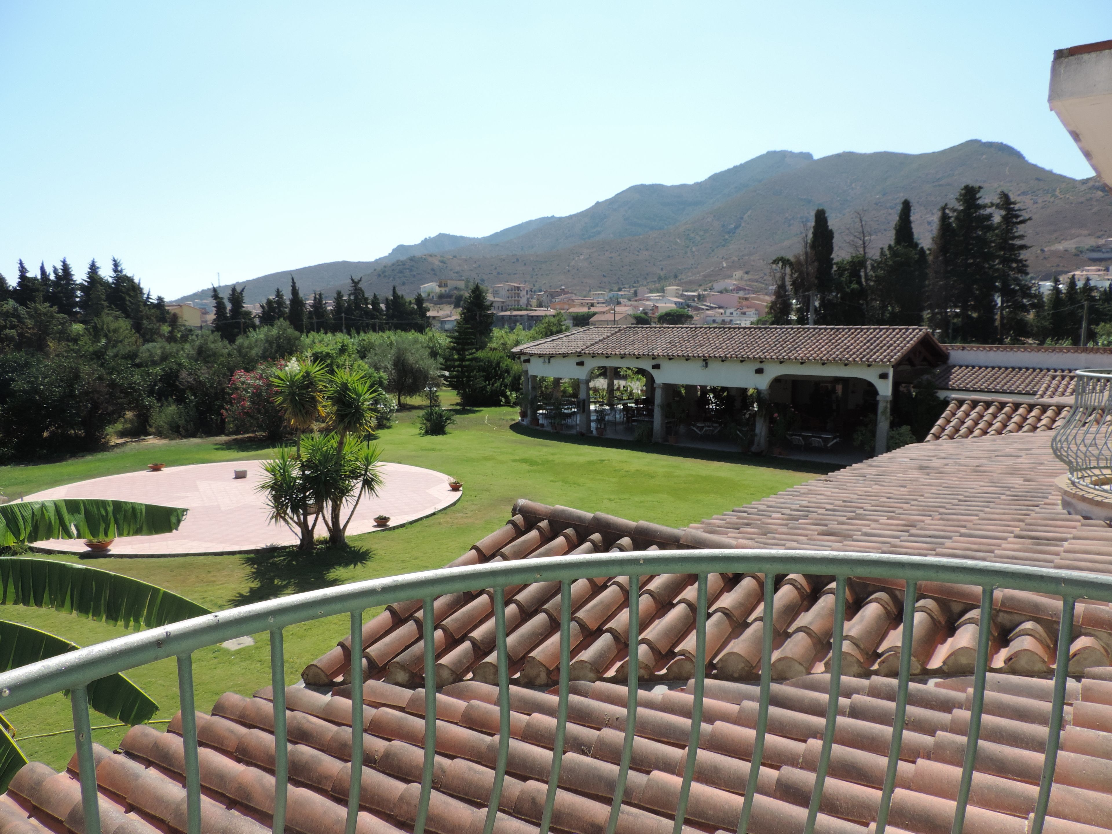 A terrace with a view of a mountainous landscape, a covered outdoor seating area, and a well-maintained garden.
