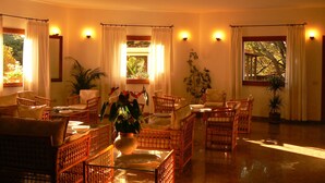 A spacious room with wicker furniture, a glass table, and potted plants. - Hotel Piccolo Golf (Arzachena)