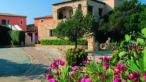 A courtyard with stone buildings, a tree, and flowering plants. - Hotel Piccolo Golf (Arzachena)