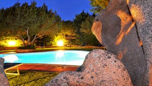A swimming pool surrounded by rocks and trees, with a chair and umbrella in the background. - Hotel Piccolo Golf (Arzachena)