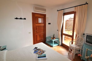 A bedroom with a bed, a small table with fruit, a chair, and a television. - Hotel Piccolo Golf (Arzachena)