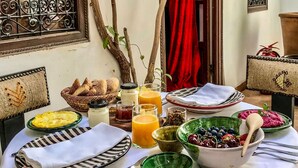 Una mesa de desayuno servida con diversos platos, entre ellos frutas, pan y bebidas.