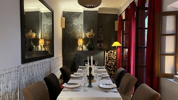 Un'area pranzo con un tavolo lungo apparecchiato per quattro persone, affiancato da sedie. Uno specchio riflette l'ambiente, e sullo sfondo si nota un camino.