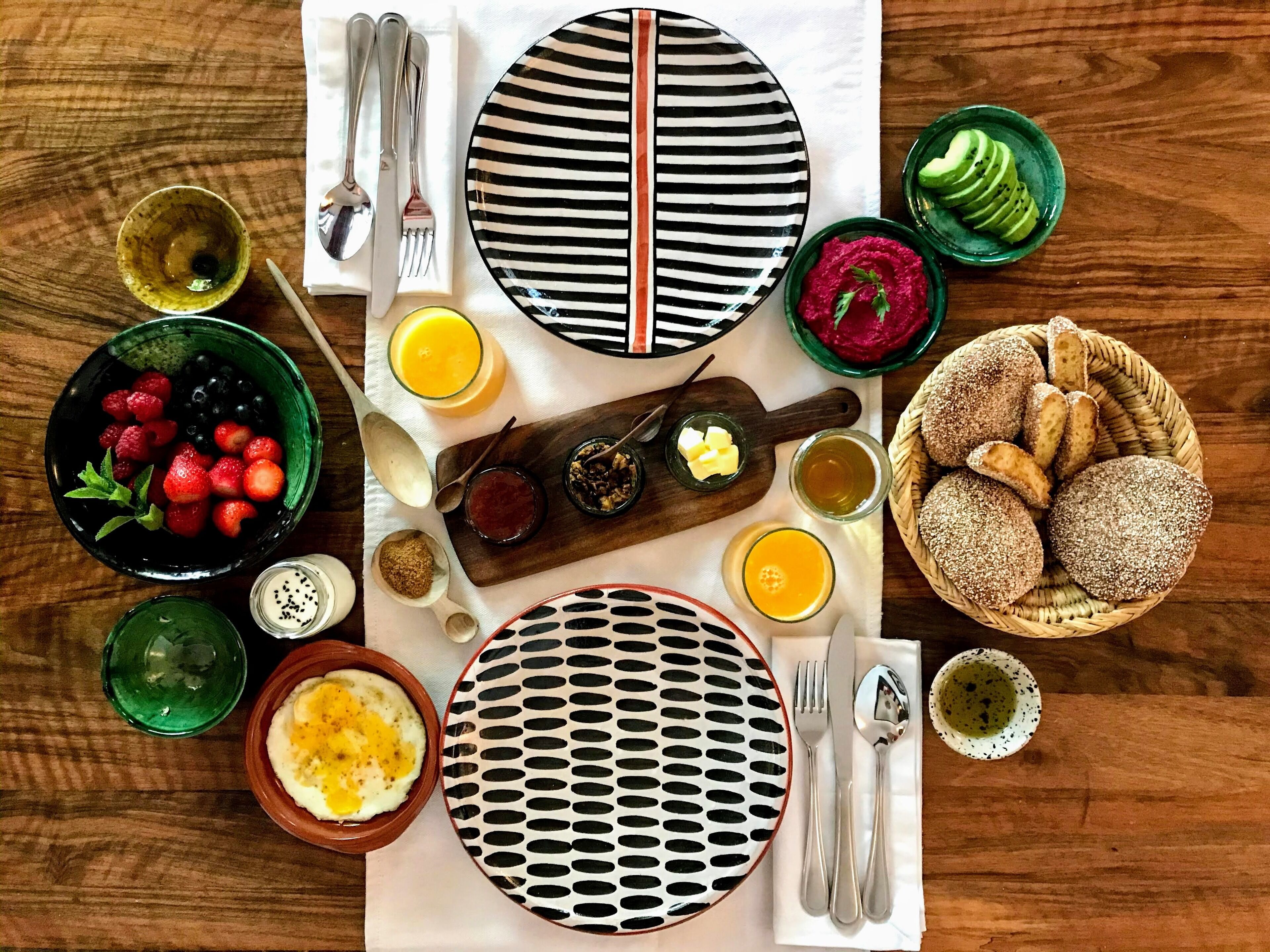 Una escena de desayuno con platos, tazones y utensilios sobre una mesa de madera.