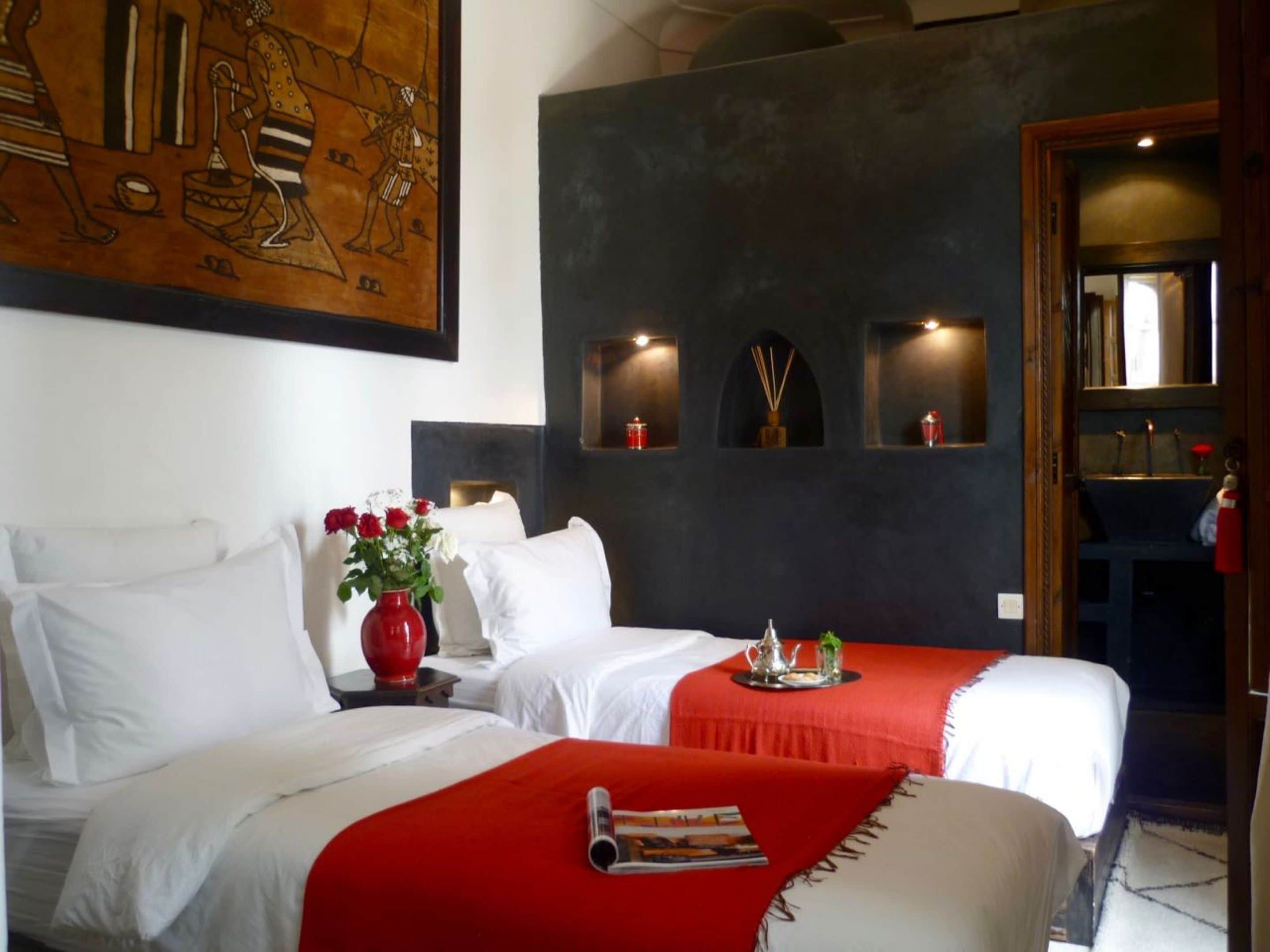 Une chambre d’hôtel avec deux lits, une décoration aux couleurs rouge et blanche, un grand tableau au mur et une petite table avec un plateau.