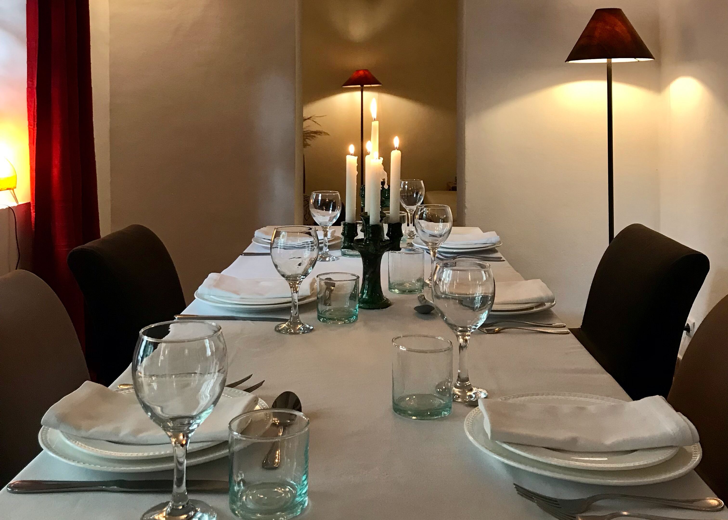 A dining table set with plates, glasses, and candles, with a lamp and a candelabra in the background.