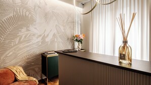 Ein moderner Empfangsbereich mit einem Holzbüro, einem kleinen grünen Beistelltisch, einer Couch und einer Wand mit einem Blattmuster.