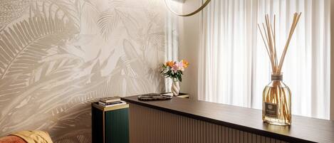 Un espace d’accueil moderne comprenant un comptoir de réception en bois, une petite table d’appoint verte, un canapé et un mur orné d’un motif de feuilles.