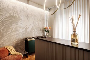 Una zona de recepción moderna con un mostrador de madera, una mesita auxiliar verde, un sofá y una pared con diseño de hojas.