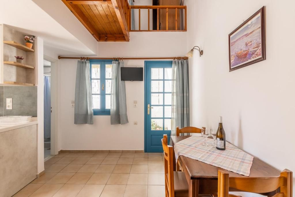 Un coin repas avec une table dressée pour deux personnes, un téléviseur fixé au mur et une porte ornée de rideaux bleus.