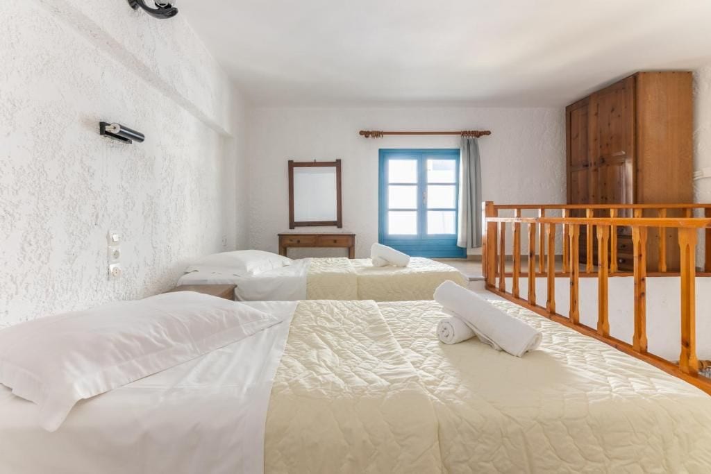 A hotel room with two beds, a wooden railing, a window with curtains, and a wooden wardrobe.